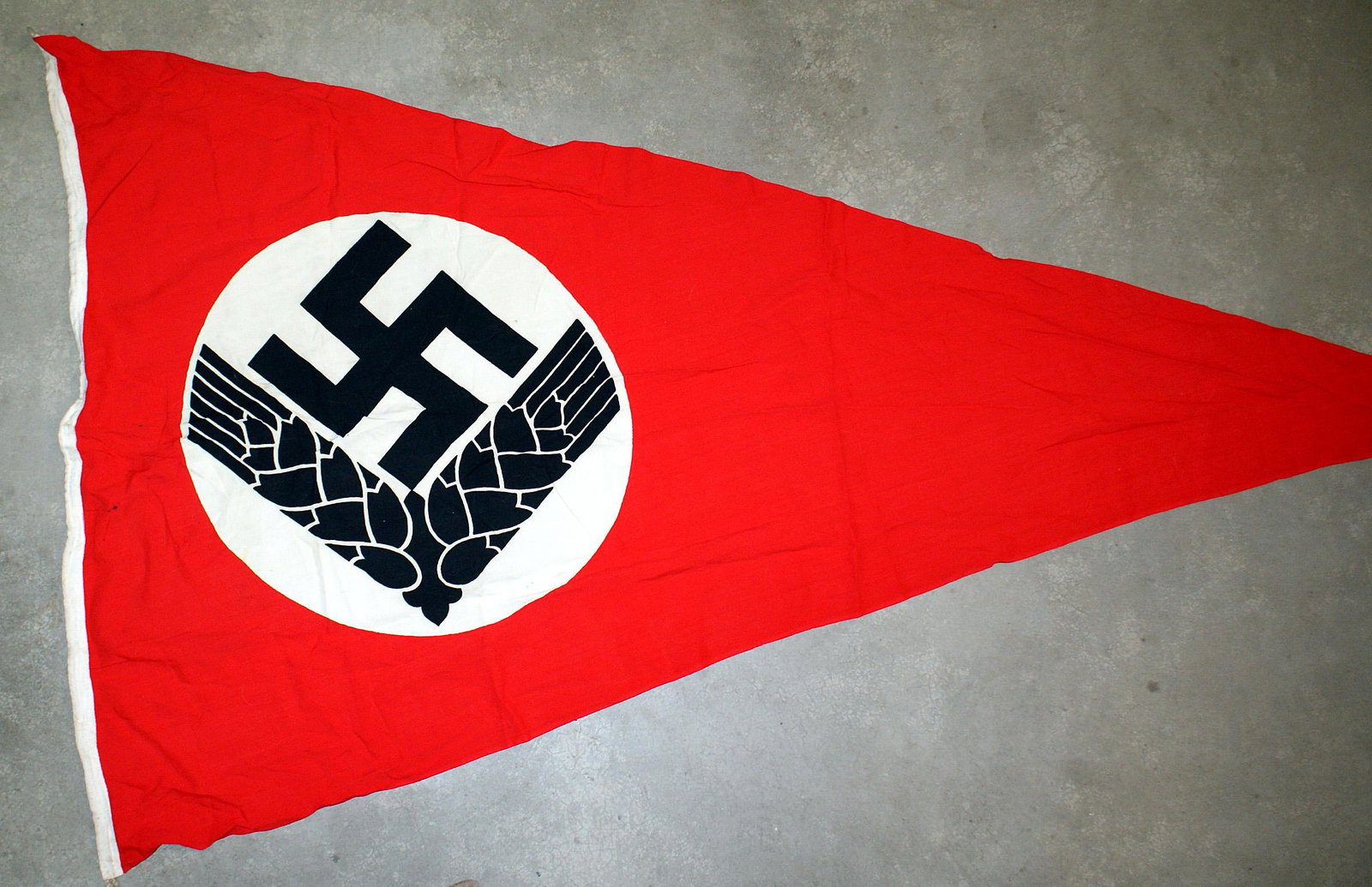 German WWII RAD National Labor Corps pennant: H-080 RAD (National Labor Corps-female) pennant. Tilted black swastika above stalks of barley on a white " diameter circle-on a red field. 48" x 82". Loops in both corners. II