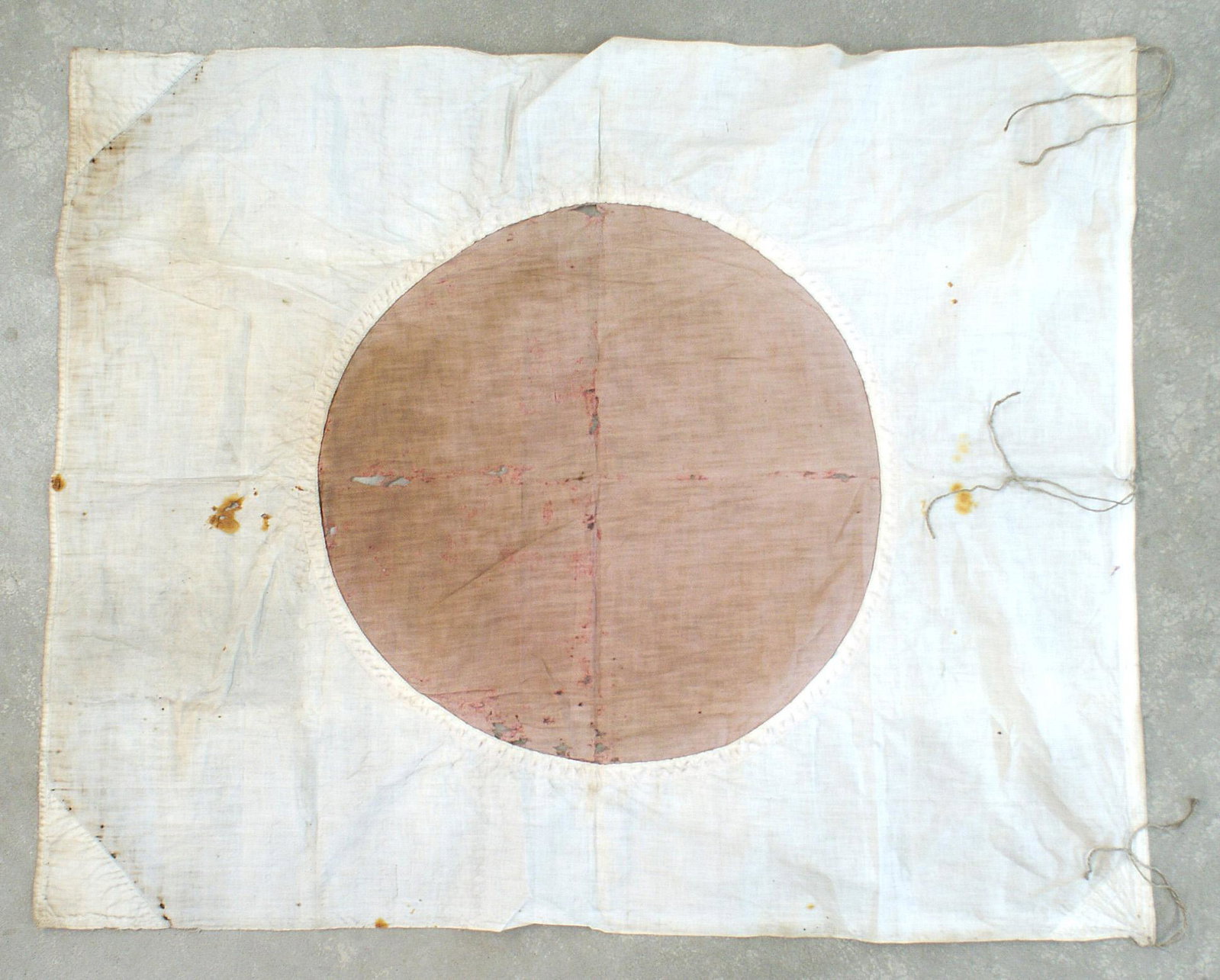 Japanese WWII cotton meatball flag: H-118 Japanese WWII cotton "meatball" flag. 20 1/2" diameter, machine - sewn red disc to opening in center of the white field. Soiled, shrapnel holes and what appears to be blood stains. Two reinforce