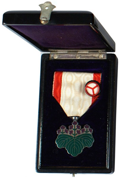 Japanese Order of the Rising Sun medal: B-291 Same - 7th Class. Green enameled pawlonia leaves with purple flowers. White/red ribbon with original black lacquered presentation case with rosette. Purple silk and velour lining. With document.