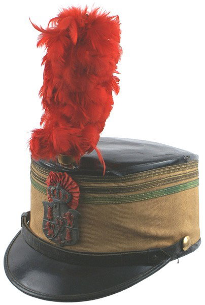 Spanish shako helmet Circa 1900: E-78 Spanish shako. Ribbed tan cloth body with two gold and one green-gold tape stripes below the crown. Black leather visor and chinstrap. Metal crowned Spanish coat-of-arms and a red rosette ribbon 