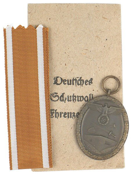 German WWII Westwall Medal: B-112 Westwall Medal with ribbon. Oval bronze with a large eagle/swastika/crossed shovel/sword above a bunker. Awarded to all personnel who helped construct Germany's West Wall fortifications. With a