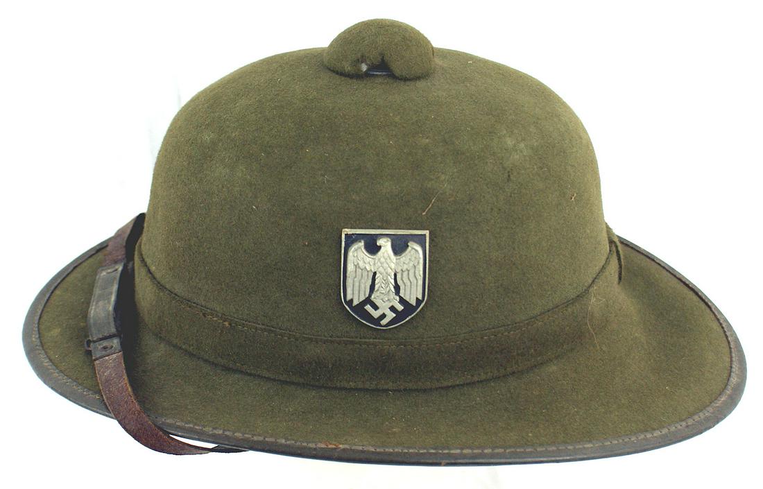 German WWII Afrika Korps pith helmet: E-012 German WWII Afrika Korps pith helmet. OD green felt body with a. leather border trim and chinstrap. Has both metal shield insignia (eagle/swastika and National colors). Leather sweatband. Shows 