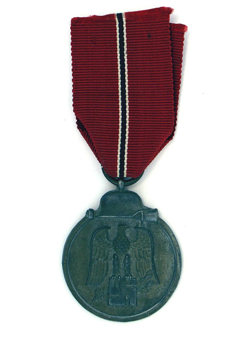 German WWII Eastern Front Medal: B-046 German WWII Eastern Front Medal. Darkened finish on a silvered perimeter with a helmet/stick grenade. Obverse bears a relief black eagle/swastika. Reverse: "MEDAL FOR THE WINTER BATTLE IN THE EA