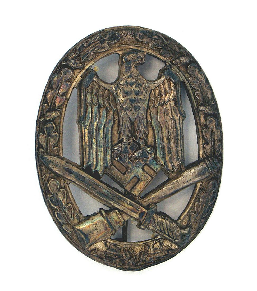 German WWII Army Waffen SS General Assault Badge: B-051 German WWII Army/Waffen-SS. General Assault Badge. Silver. Open oak leaf wreath holding an eagle/swastika and crossed bayonet/stick grenade. Solid type with an aged patina. Reverse is slightly d