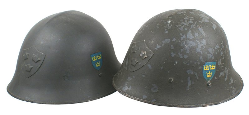 Lot of 2 Swedish WWII helmets: E-83 Lot of 2 Swedish WWII helmets: (1) Three crowns on a shield applied to front and some yellow-gold on blue decals on sides. OD finish shows chips. Three double-tongue pad holder liner. With chinst