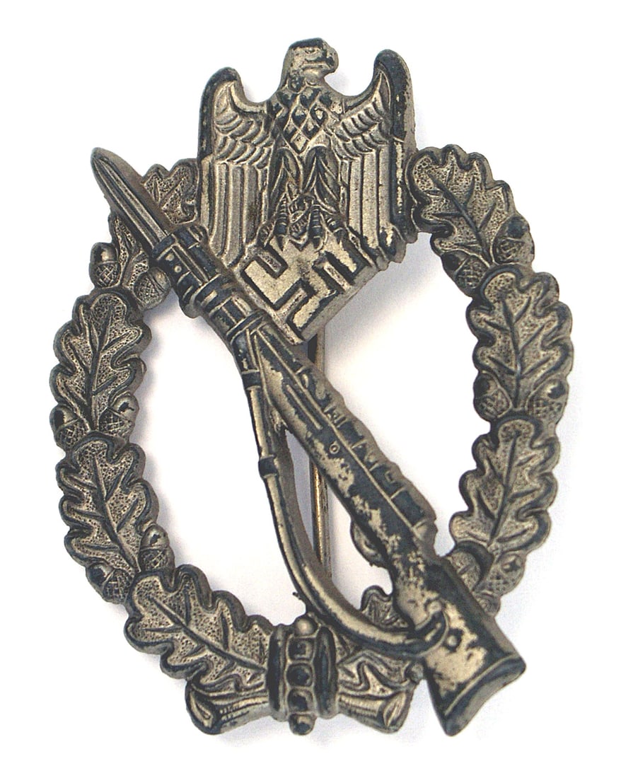German WWII Infantry Assault Badge Silver: B-058 German WWII Infantry Assault Badge - Silver. Eagle/swastika at top of an open oak leaf wreath - holding a rifle with a fixed bayonet. Stamped variety. Solid, lightweight and has most of the silv