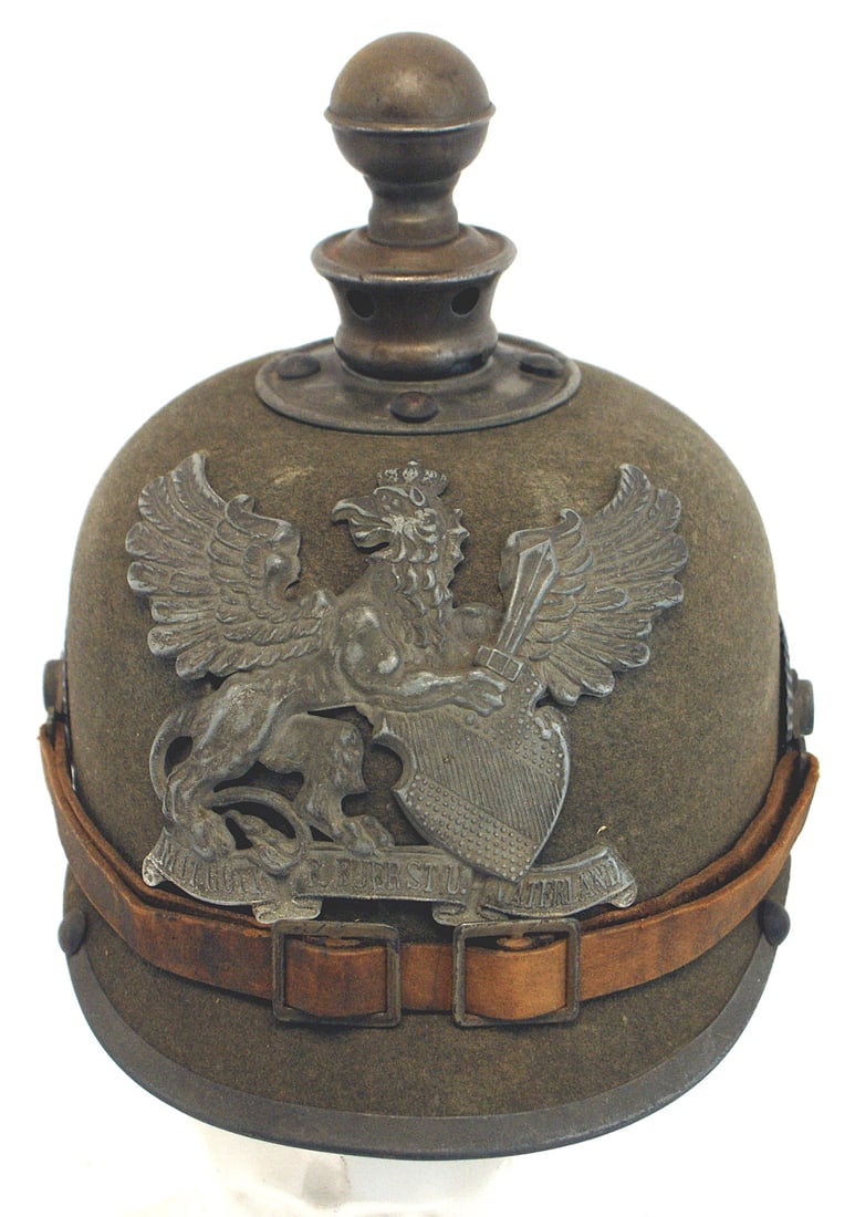 Baden WWI felt EM Artillery helmet: E-010 Baden WWI felt EM Artillery helmet. Solid perfectly shaped body with a gray griffen/sword/shield/motto Coat-of-Arms front plate. Also a gray two-piece ball-top/base. Visor trim and fittings. Int