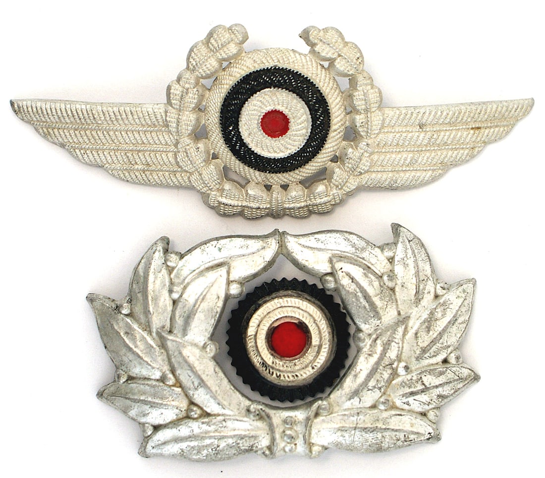 German WWII peaked cap insignia DLV TN: E-166 Lot of 2 Third-Reich peaked cap insignia: (1) DLV - short winged wreath/rosette. (2) TN - squared linden leaves wreath with a rosette. II