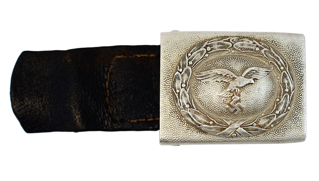 German WWII Luftwaffe EM belt buckle: H-005 German WWII Luftwaffe EM aluminum belt buckle. Pebbled finish with a relief flying eagle/swastika within an oak leaf wreath. Reverse marked "...39". Leather tab shows wear. II