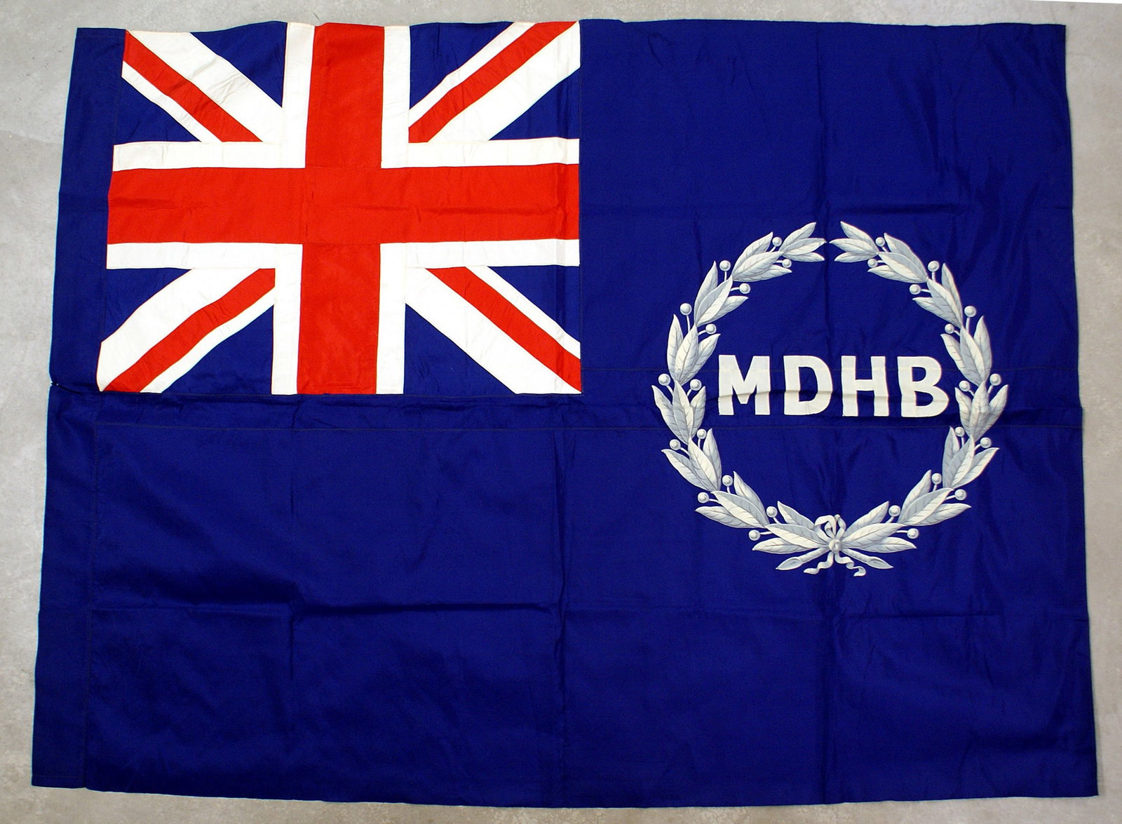 Royal British Mersey Docks and Harbor Flag: H-138 Royal British Mersey Docks and Harbor Flag. All silk, with a 26" x 31 1/2" multi construction Union Jack in the upper left corner. The right side has a 23" x 23" silver gray laurel wreath holdin
