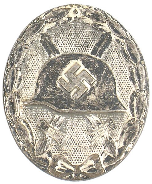 German WWII Wound Badge Silver: B-123 German WWII Wound Badge-Silver. Solid type. Relief helmet with a large swastika and crossed swords on a stippled background within an oak leaf perimeter. Reverse marked "100" (firm of Rudolf Wac