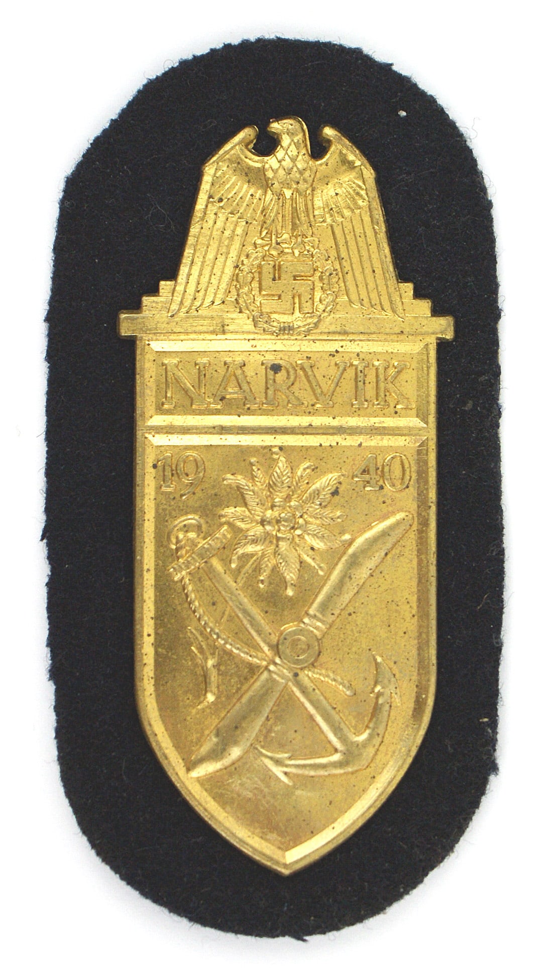 German WWII Navy NARVIK Shield Gold: B-052 German WWII Navy "NARVIK" Gold Sleeve Shield. Large eagle/swastika over "NARVIK", "1940", an edelweiss and a crossed prop/anchor. Nice patina. Navy blue cloth background and paper on reverse. II