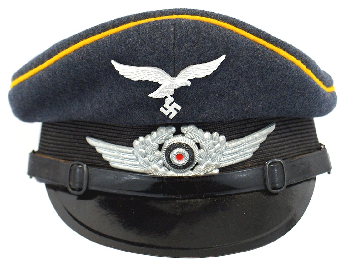 German WWII Luftwaffe Flight Units peaked cap: E-056 German WWII Luftwaffe E.M./NCO Flight Units peaked cap. Yellow-gold piped blue-gray wool body with a ribbed black cloth band. Black leather chinstrap. Metal eagle/swastika and winged rosette ins