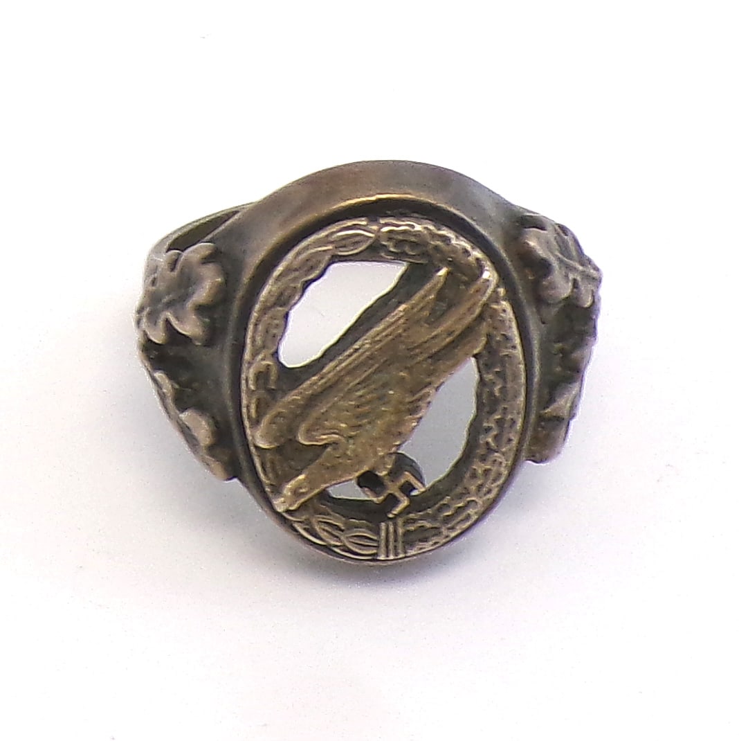 German WWII Luftwaffe paratrooper ring: H-057 German WWII Luftwaffe paratrooper ring. Age darkened silvered body with applied oak leaves on the sides. Miniature of a cut-out paratrooper badge is mounted on center which has a matching cut-ou