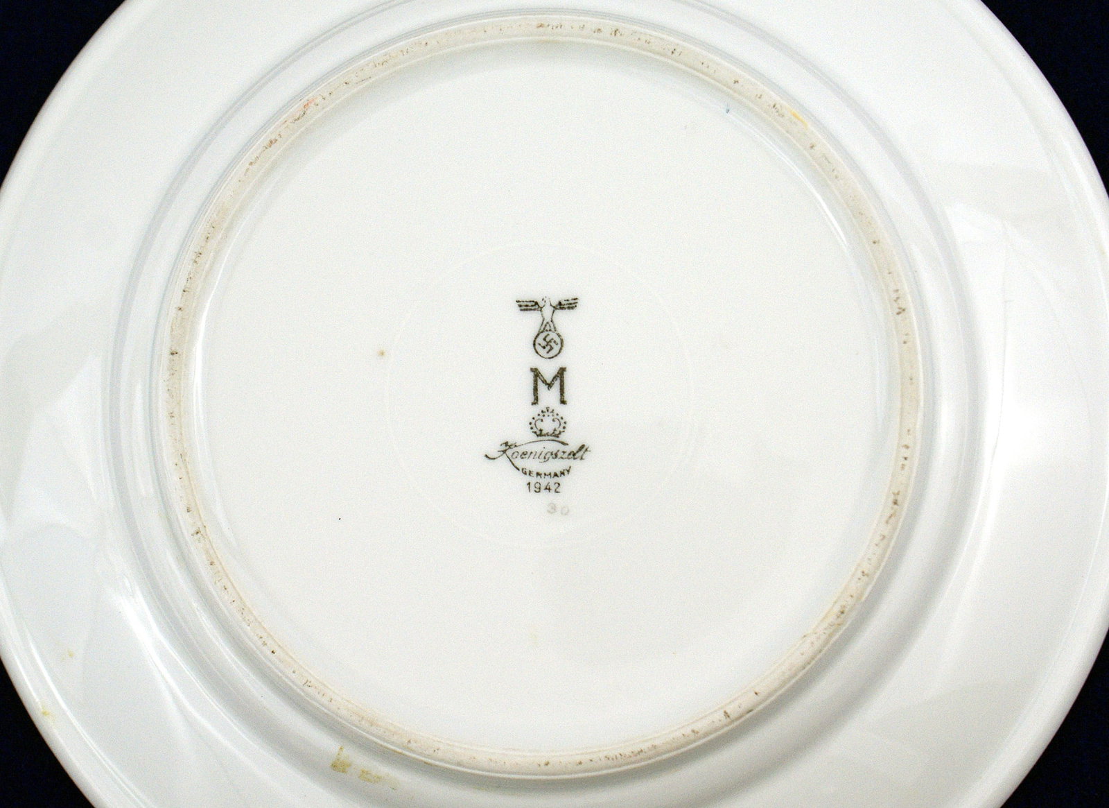 German WWII Navy mess hall porcelain dinner plate: H-064 Third-Reich Navy mess hall Porcelain dinner plate. Linear red inner border. 9 5/8" diameter. Reverse marked with eagle/swastika, "M" and name of maker "Koenigszdt...1942". From the Donald G. Bro
