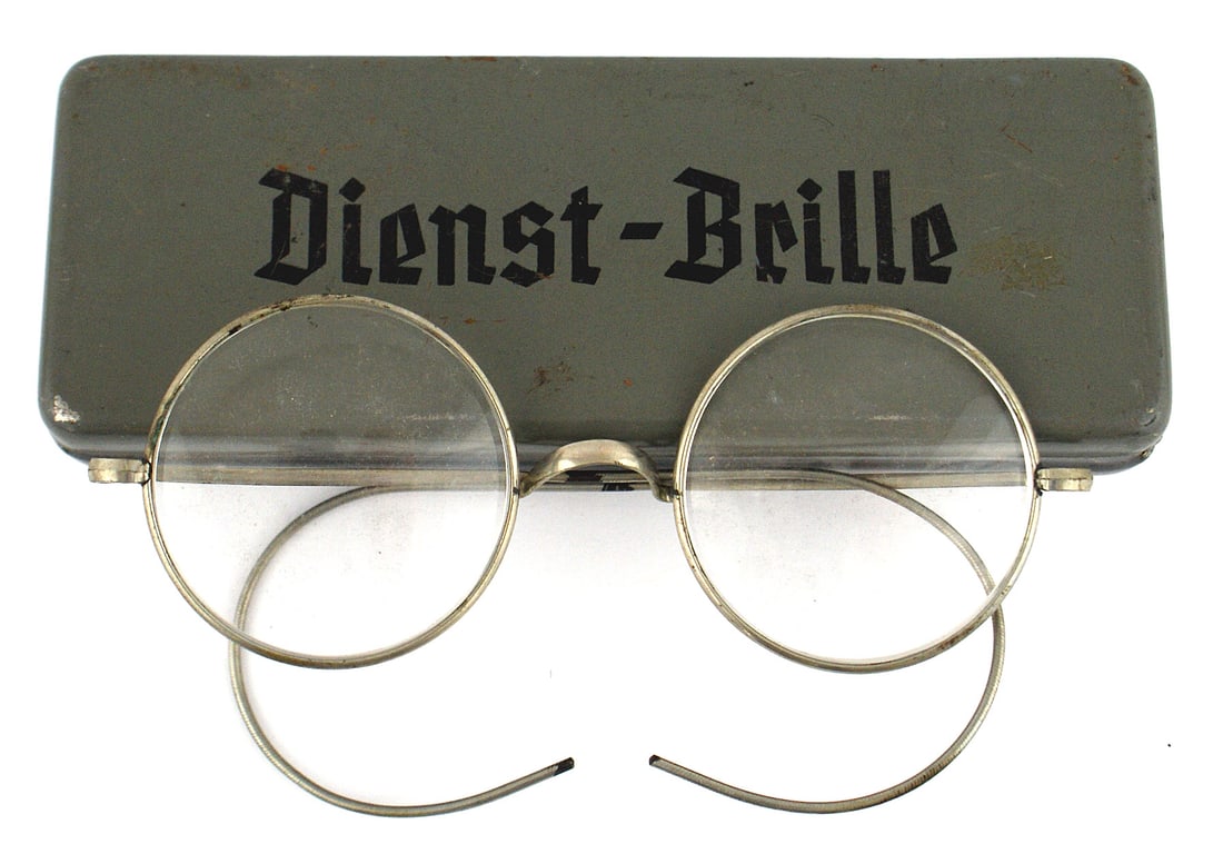 German WWII Dienst Brille gas mask glasses: N-003 German WWII "Dienst-Brille". Black ink print on hinged lid of metal case. Wire rimmed glasses to be worn with gas mask. With name tag of a Paymaster serving with the 380th Battalion. Dated "13.1
