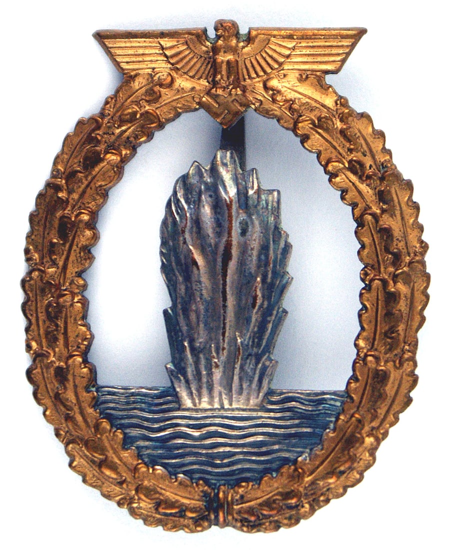 German WWIII Navy Minesweeper Badge: B-060 German WWIII Navy Minesweeper Badge. Gilt eagle/swastika at top of an open oak leaf wreath. Center holds an upward spray of silver water. Age-toned flat reverse is marked "R.K." A nice badge sti