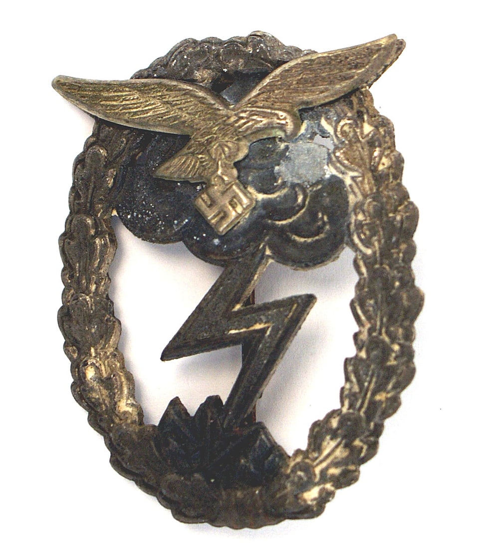 WWII Luftwaffe Ground Combat Badge: B-065 German WWII Luftwaffe Ground Combat Badge. Separately applied silvered flying eagle/ swastika on a silvered oak leaf wreath with gray clouds/ lightning bolt. Wreath partially darkened. Round ver