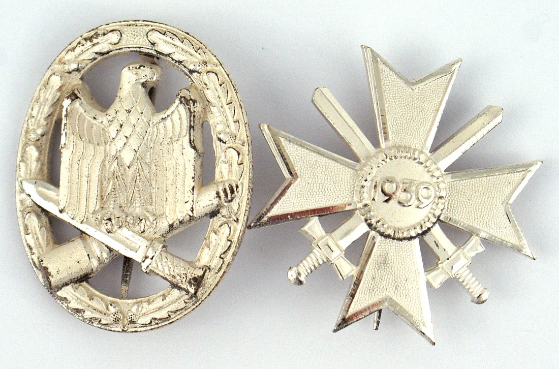 Lot of 2 German 1957 awards Assault Badge KvK: B-090 Lot of 2 German 1957 produced versions of German awards of WWII. Both fairly identical but lacking a swastika. Includes: (1) General Assault Badge. Silvered oak leaf wreath holding an eagle on a
