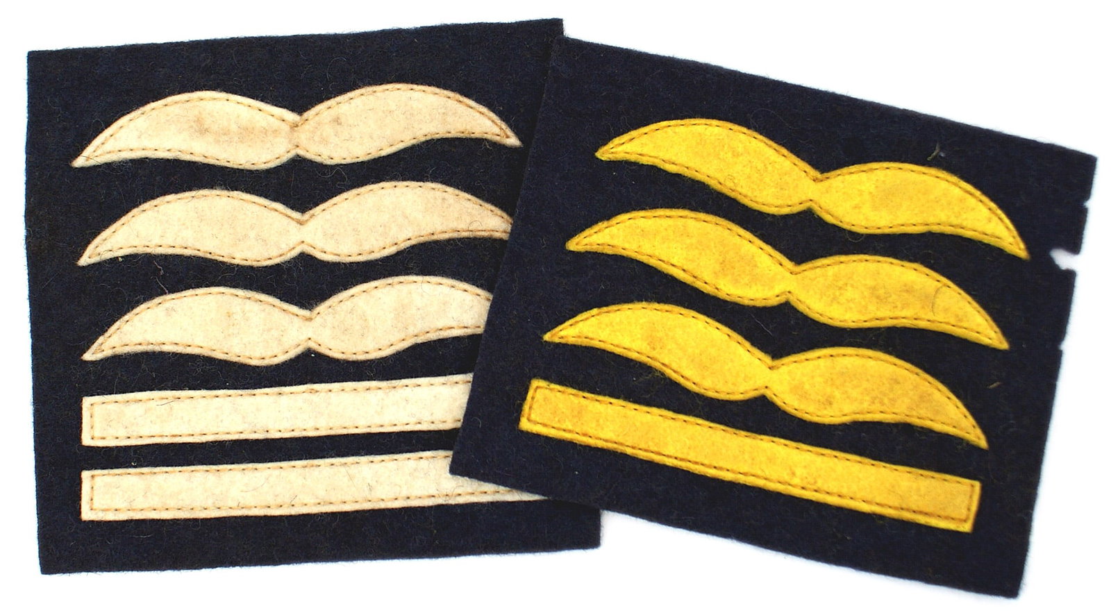 German Luftwaffe WWII flying suit rank insignia: H-043 Two examples of German Luftwaffe WWII flying suit rank insignia: (1) Oberst. Three white felt wings above two bars on a blue field. (2) General Flieger. Three felt yellow-gold wings sewn above o
