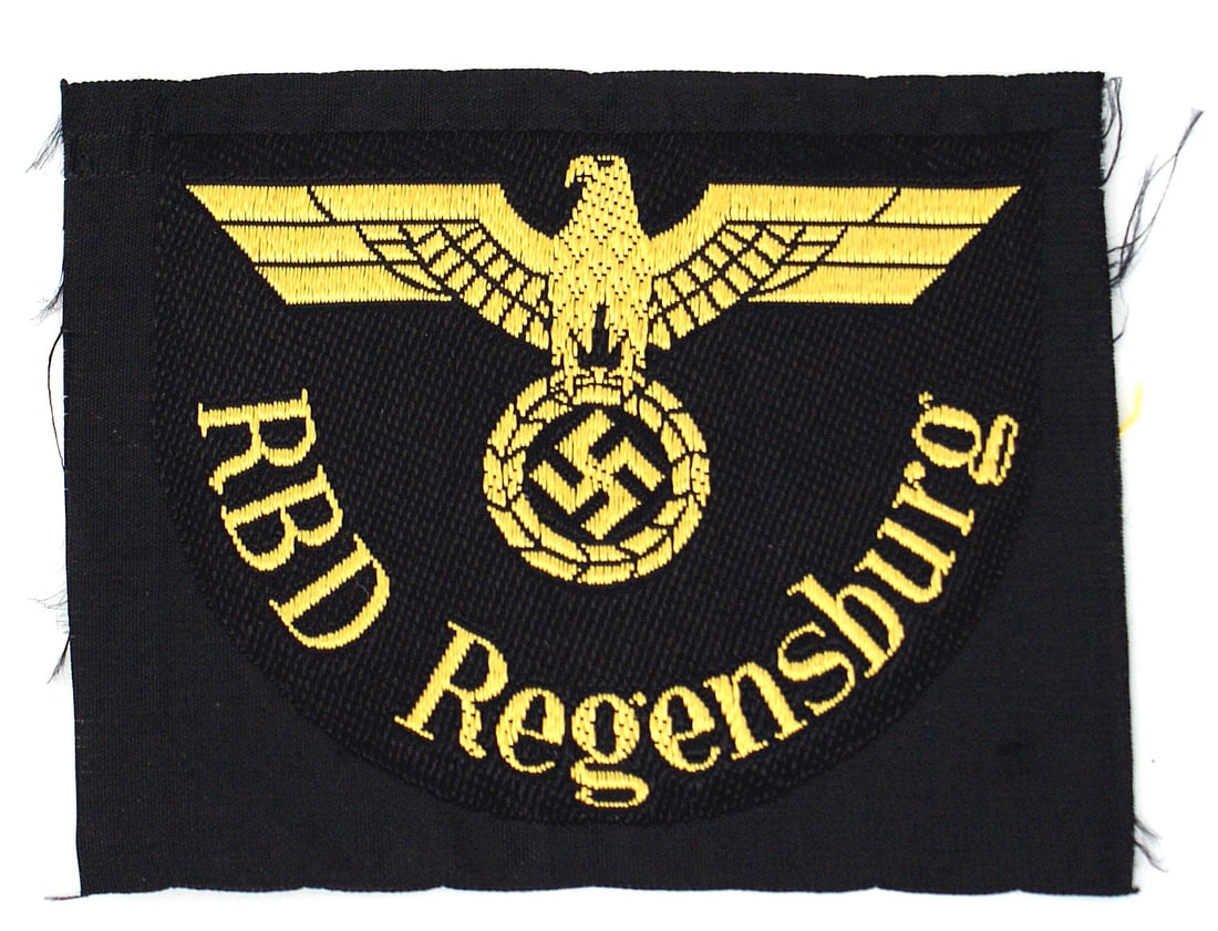 German WWII State Railway sleeve insignia Regensburg: H-053 German WWII State Railway Directorate members tunic sleeve insignia for Regensburg. Bevo embroidered gold silk eagle/swastika above "RBD" Regensberg" on black underlay. Uncut. II+