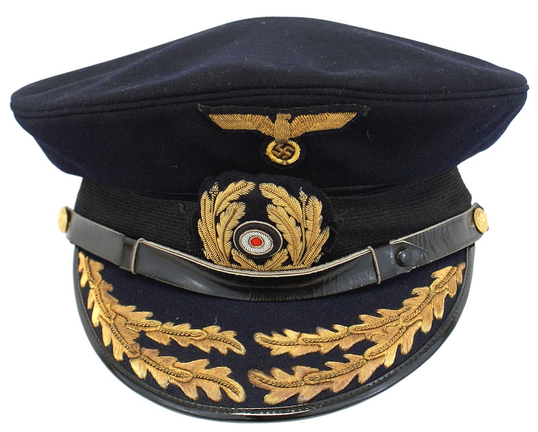 German WWII Navy Vice Admiral peaked cap: E-063 German WWII Navy Vice Admiral peaked cap. Quality dark blue body with a black mohair band. Two rows of high relief embroidered gold bullion oak leaves on the brim. Black leather chinstrap with g