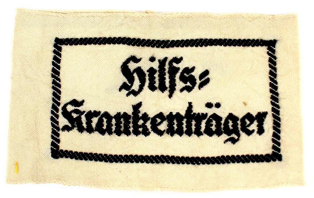 German WWII Stretcher Bearer armband: H-030 German WWII "Hilfs-Krankentrager" (Stretcher Bearer) armband. Embroidered black lettering within a black frame on a white band. II