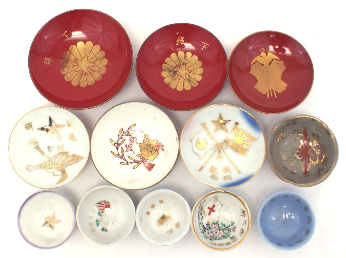 12 Japanes WWII sake saki cups: H-098 Lot of 12 Japanese WWII sake cups. Includes: (1) Nine porcelain (Red Cross flag, gilt Navy veterans badge, four with war flags, three miscellaneous) (2) Three red lacquered with gilt motifs: Ord
