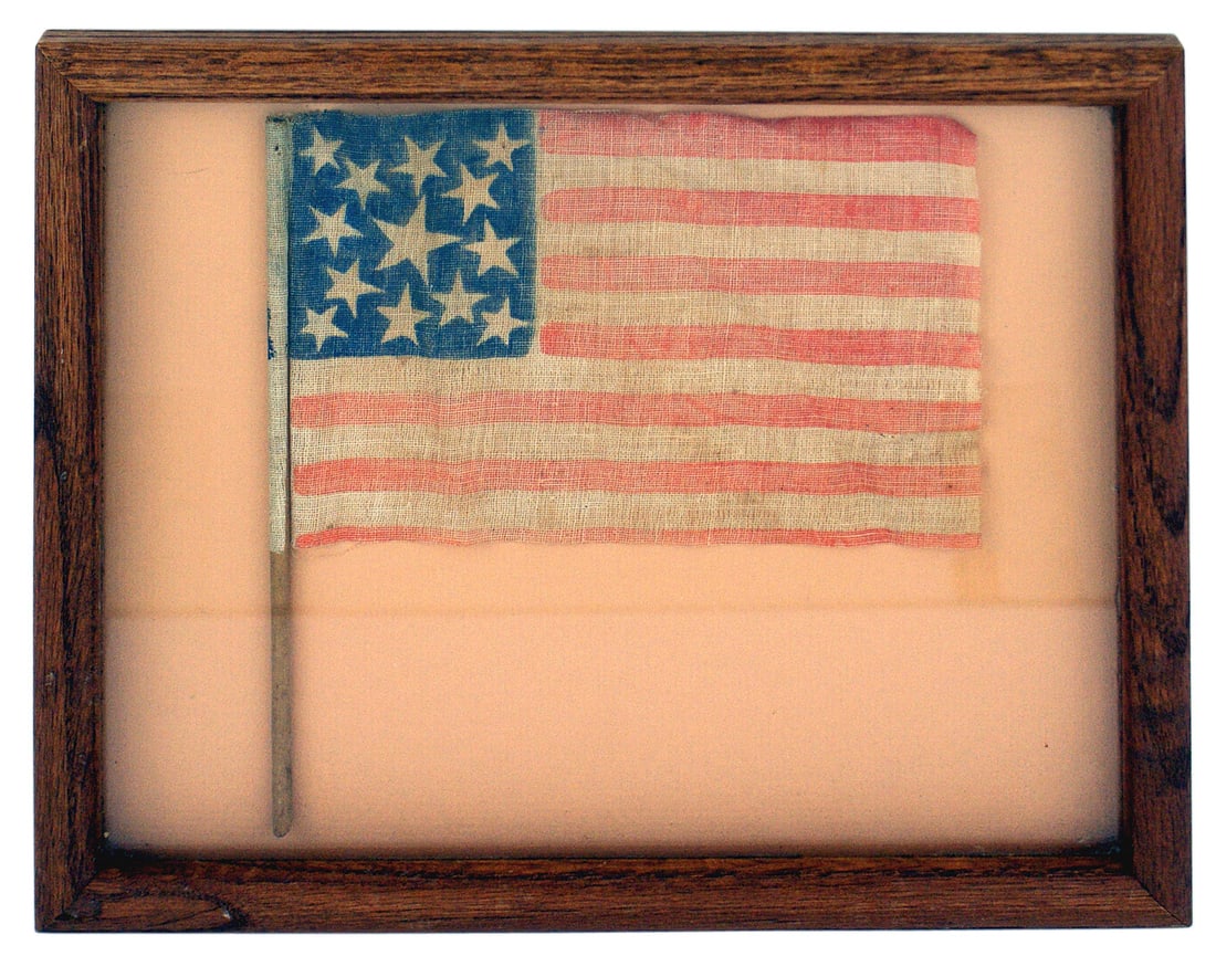 American framed 19th Century parade flag: K-098 American framed 19th Century parade flag. Blue canton has one large printed white star surrounded by 12 smaller stars. Printed off-white field has seven printed red stars. The off-white field ha