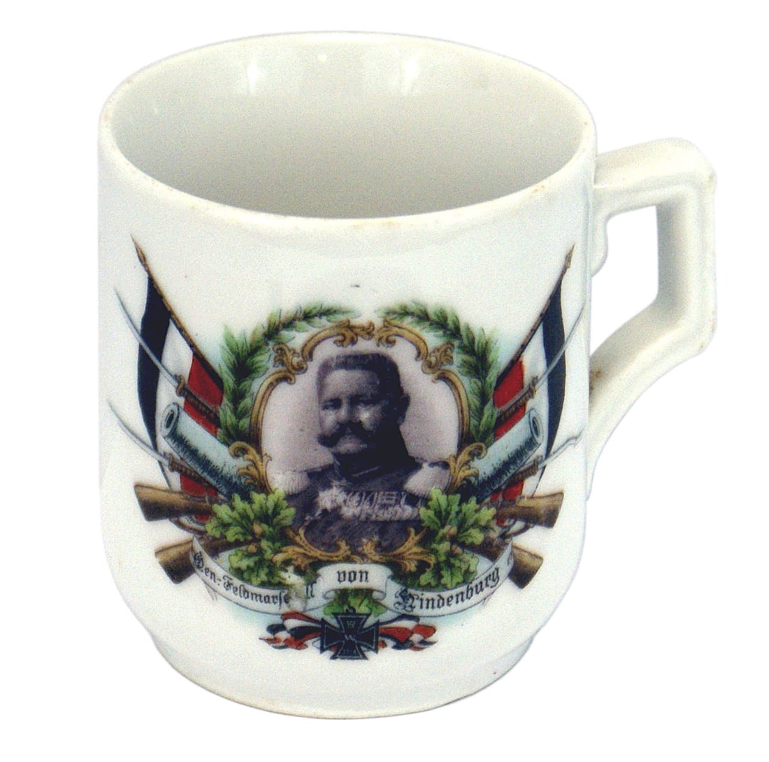 German WWI patriotic tea cup von Hindenburg: G-002 German WWI patriotic porcelain tea cup. 3" tall with a squared-off "ear". Medal laden photo of "Feldmarscall von Hindenburg" within an oak leaf wreath with crossed rifles and flags. Bottom has t