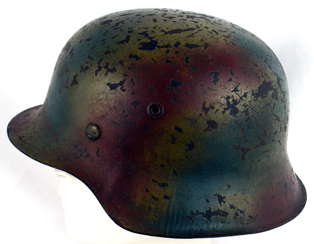 German WWII M1942 camo Normandy helmet: E-019 German WWII M1942 camouflaged "Normandy" helmet. Large irregular patches of red/tan/ochre/red. Scattered paint chips showing the age to the exposed metal. Leather tan liner shows some wear. Orig