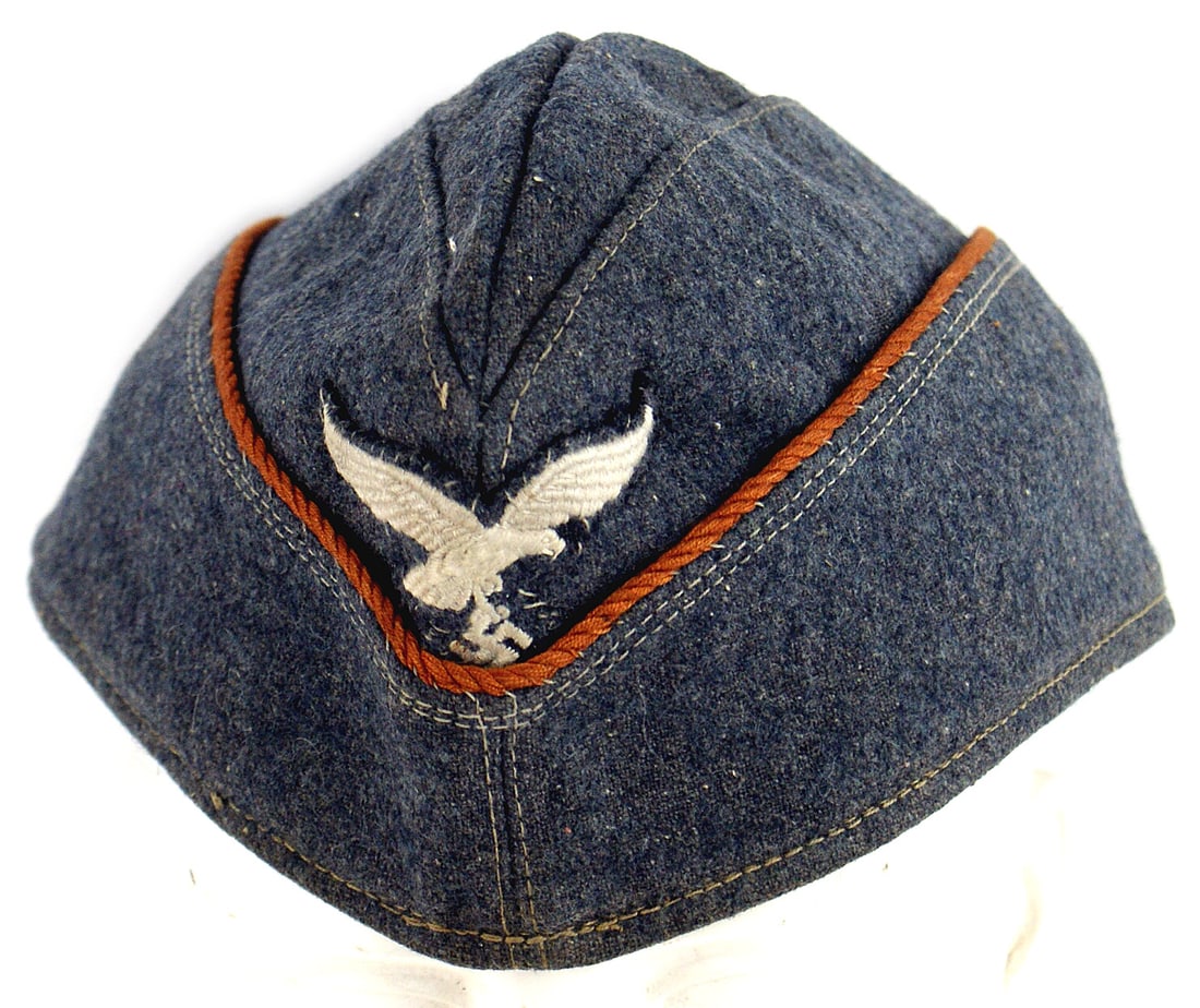 German WWII Luftwaffe EM overseas cap: E-038 German WWII Luftwaffe E.M. o'seas cap. Blue-gray wool with cinnamon cord piping (Signal Troops). Embroidered flying eagle/swastika sewn to front. I.D. letters "A. B." sewn to satin type blue-gra