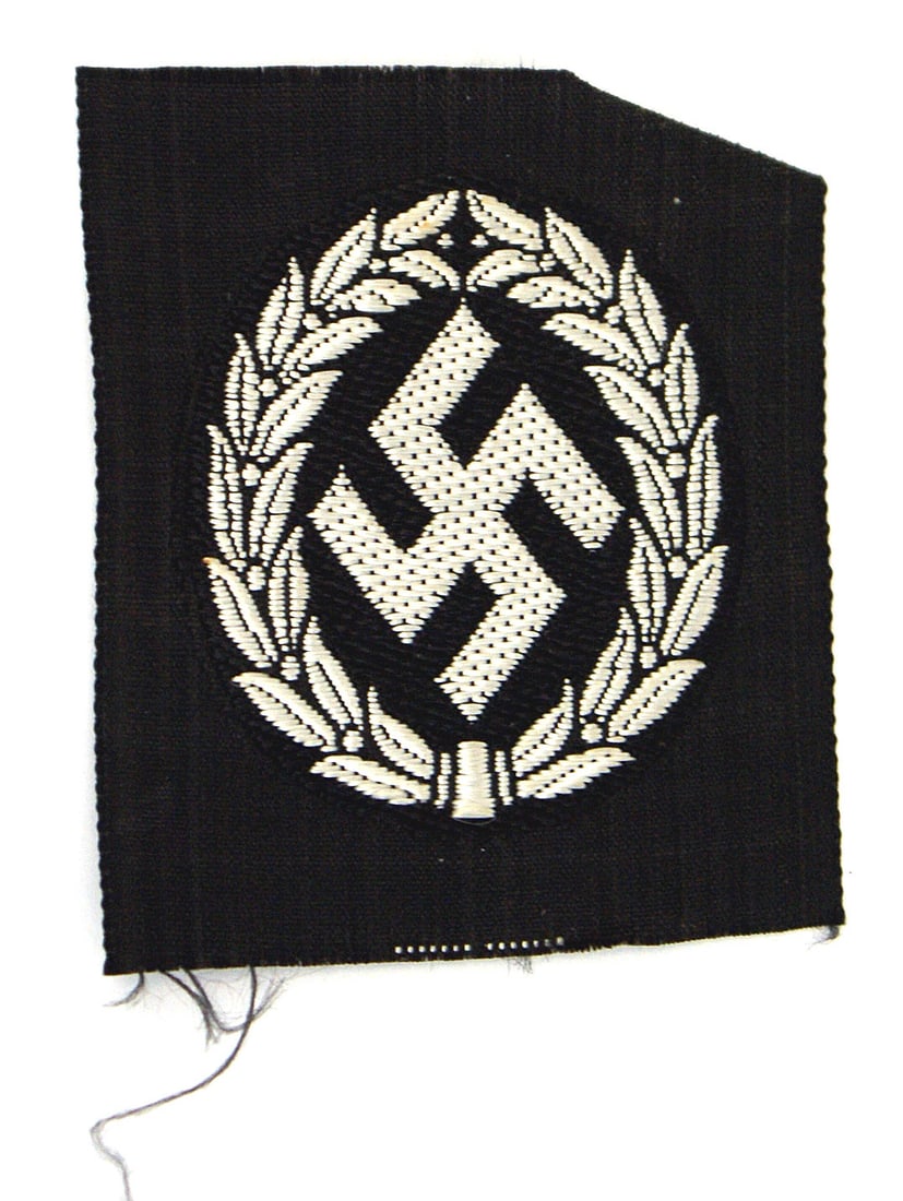 German WWII Schutzmannschaft cap badge: E-049 Schutzmannschaft officer's cap badge. Bevo type embroidered tilted silver swastika within a laurel wreath on black backing - uncut. (Recruited from anti-Communists in the German occupied Easter 