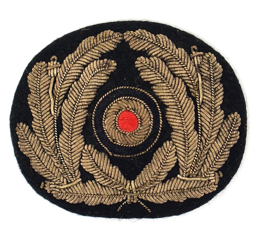 German WWII Navy Admin peaked cap insignia: E-051 German WWII Navy Administration officer peaked cap insignia. High relief embroidered silver bullion oak leaves/rosette (padded). Nice patina. II+