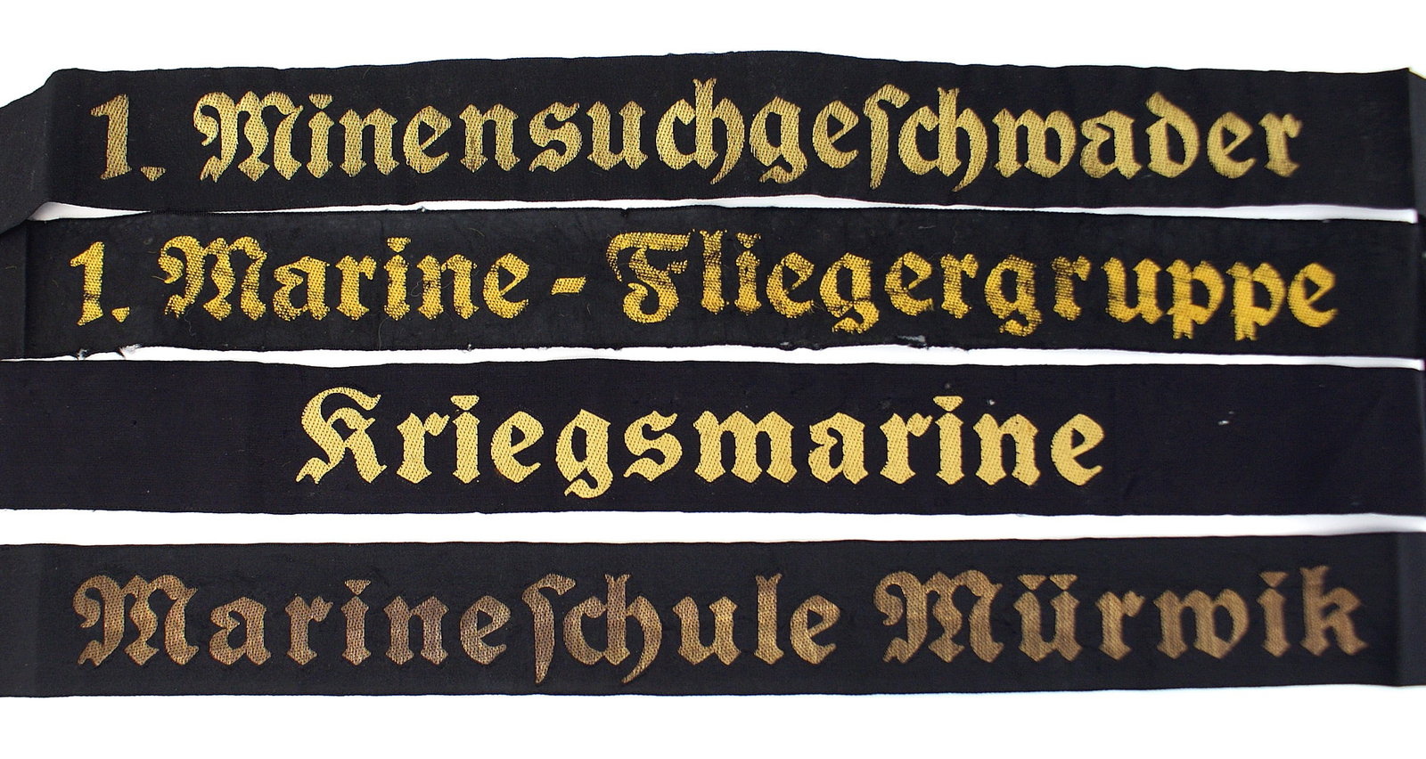 4 German WWII Navy cap tallies: E-052 Lot of 4 German WWII Navy cap tallies. All black ribbons have the unit in flat gold thread lettering. (1) "Kriegsmarine". Full ribbon has some mothing towards the ends. (2) "Marineschule Murwik"
