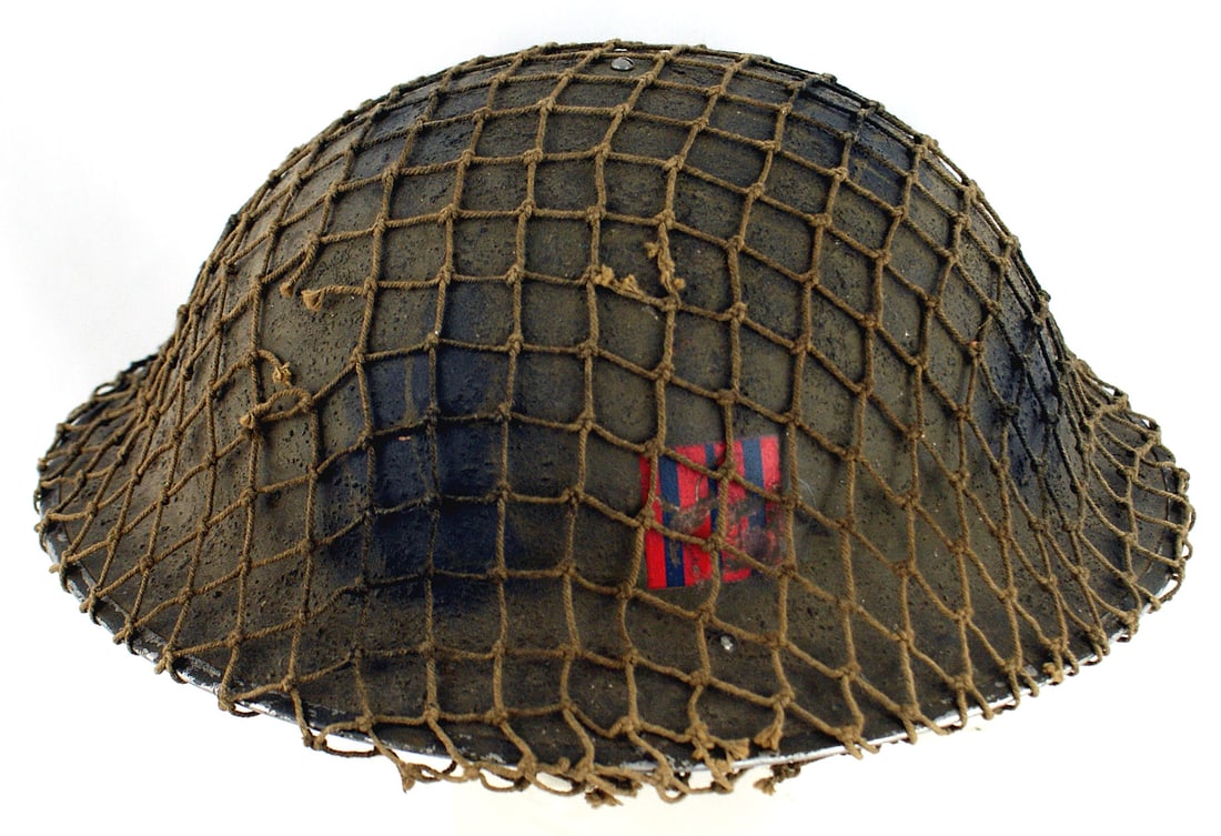 British Canadian WWII type helmet: E-067 British/Canadian WWII type helmet. O.D. sand finish with an O.D. camouflage net. Rubberized 5-tongue black liner. Right side of helmet has a blue rectangle with two capital "HH" letters in red. 