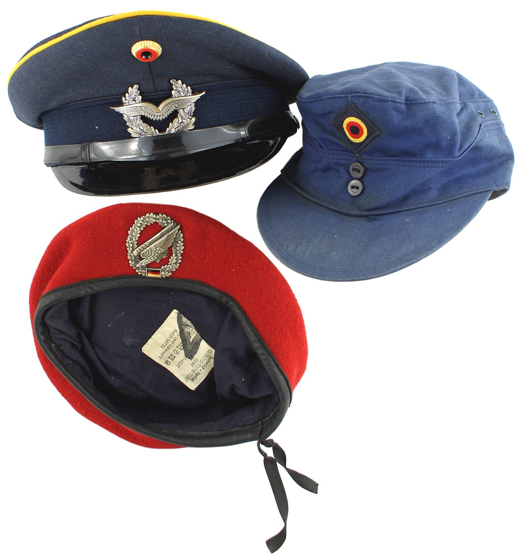 Lot of 3 examples of West German caps: E-082 Lot of 3 examples of West German head gear: (1) Air Force E.M. Flight Troops peaked cap. Dark blue body and band with yellow-gold piping. Black laminated visor and simulated leather chinstrap. L