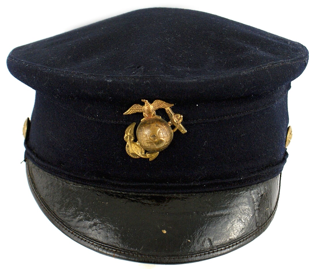 Marine Corps M1902 EM peaked cap: E-093 Marine Corps M1902 EM peaked cap. Brass EGA badge. Entire cap is dark blue with a black leather brim. Underside leather is torn. Leather sweatband shows wear and age. Gilt eagle/anchor side butt