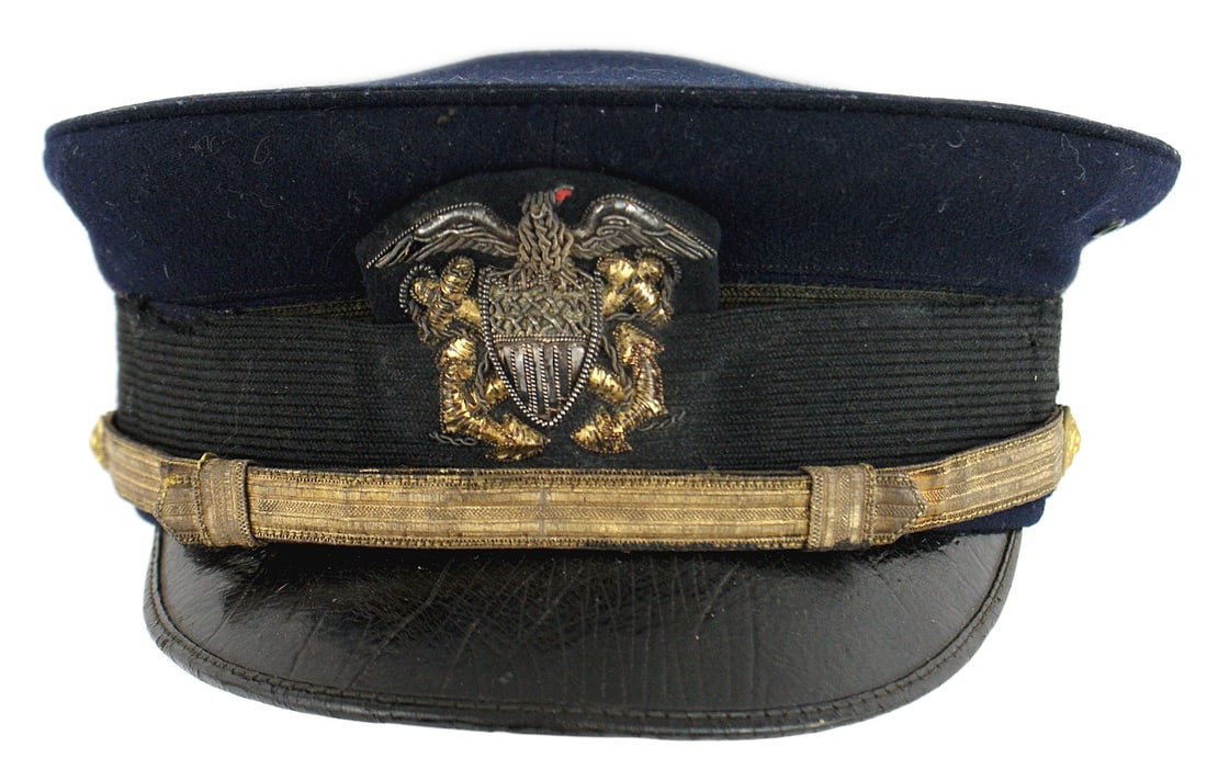 US Navy WWI officer peaked cap: E-095 US Navy WWI officer's peaked cap. Dark blue body with a black mohair band (with several pulls). Gold and silver, relief embroidered US eagle/shield/crossed anchors. Black leather brim. Some age 