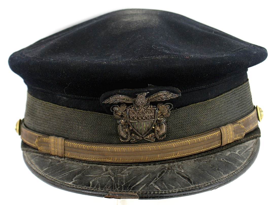 US Navy officer dark blue peaked cap: E-096 US Navy officer's dark blue peaked cap. Black leather brim and mohair cap band. Relief embroidered gold bullion anchors, American Shield and eagle insignia. Gold cap chinstrap. Leather sweatband