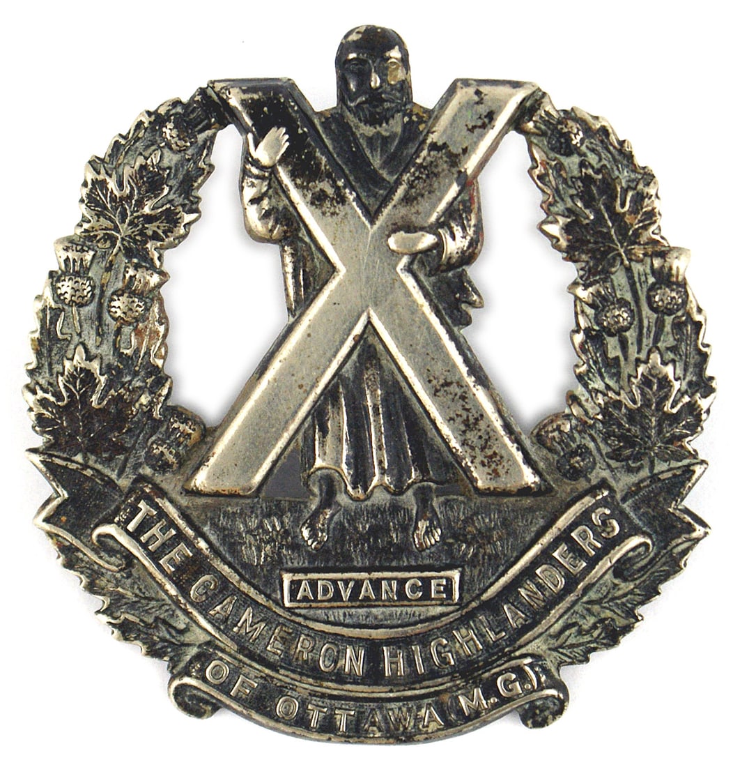 Canadian WWII CAMERON cap badge: E-103 Canadian WWII "CAMERON HIGHLANDERS OF OTTOWA M.G." cap badge. St. Andrew holding an "X" shaped cross in an open wreath of thistle and name of unit. Silvered finish shows darkened age patina. Rev