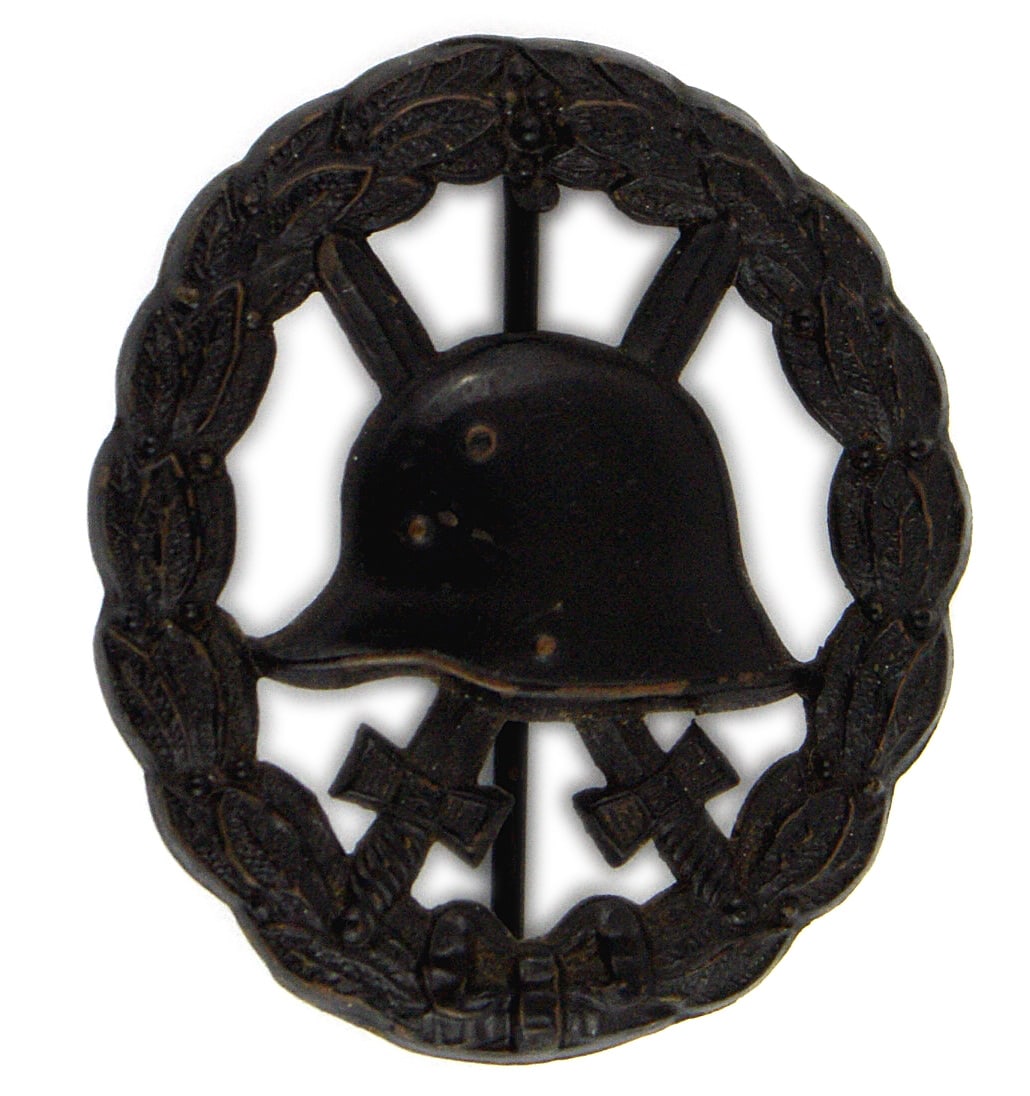 German WWI Wound Badge Black: B-016 German WWI Wound Badge - Black. "Swank" type - cut-out helmet with crossed bayonets in center of an open oak leaf wreath. I