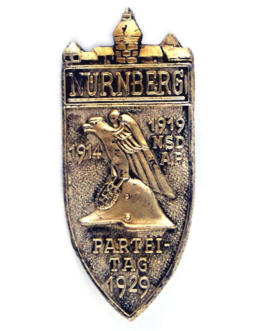 German WWII Nurnberg Party Day Badge: B-022 Third-Reich Nurnberg Party Day Badge. Age toned silver, with a shield shape, bearing an eagle perched on a swastika decorated helmet. Also "NURNBERG 1914 - 1919 NSDAP - PARTEITAG 1929". Pin-back