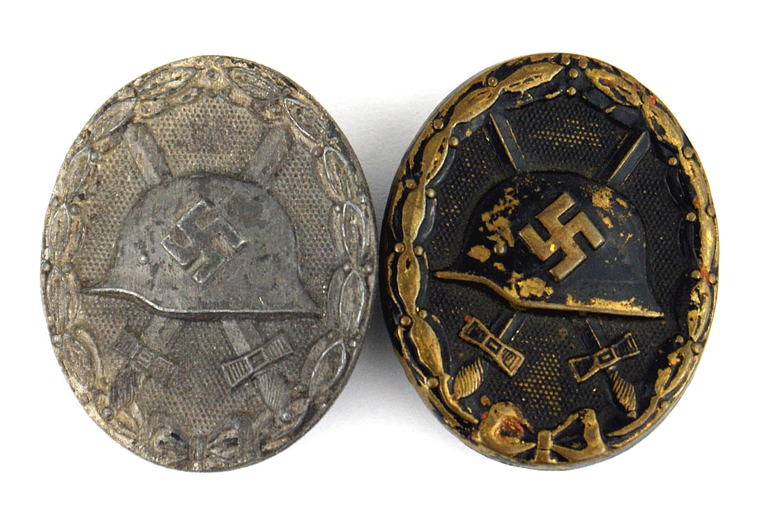 2 German WWII Wound Badge Black Silver: B-063 German Third Reich WWII Wound Badges: (1) Black - relief helmet with a swastika with crossed swords on a pebbled background with an oak leaf wreath perimeter. 50% of black finish. (2) Silver. Sa