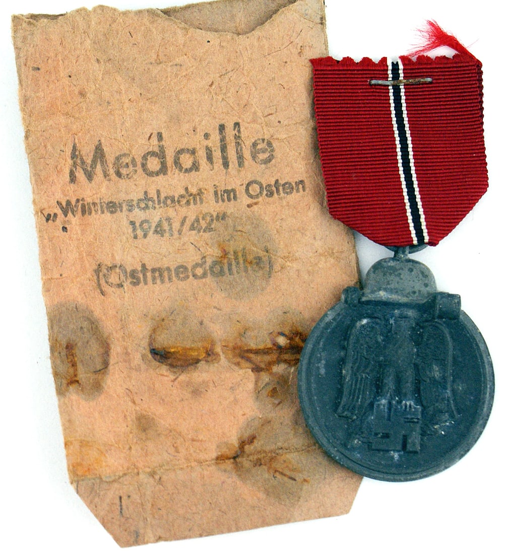 German WWII Eastern Front Medal: B-069 German WWII Eastern Front Medal. Helmet/stick grenade above a relief eagle/swastika. Awarded for military service in Russia. With ribbon and unmarked ring. Original paper packet envelope is stam