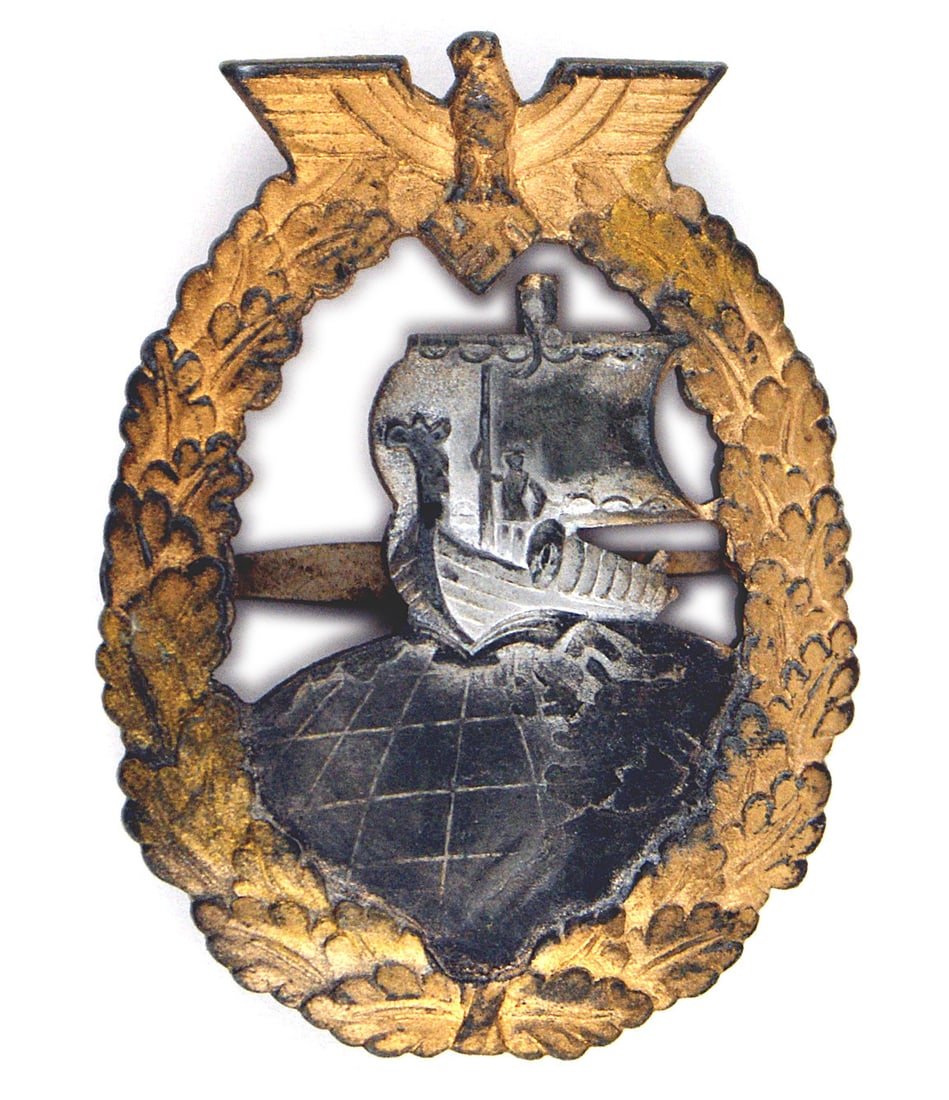 German WWII Navy Auxiliary Cruiser Badge French: B-073 German WWII Navy Auxiliary Cruiser Badge. Made by the French firm of Baqueville. Eagle/swastika at top of an open gold oak leaf wreath. Viking ship in center was silver which has grayed and glob