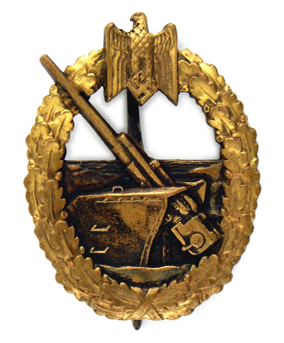 German WWII Navy Coastal Artillery Badge: B-079 German WWII Navy Coastal Artillery Badge. Open type gold-brass oak leaf wreath/eagle at top with silvered coastal gun. Reverse has name of maker "FEC OTTO PLACZEK - BERLIN AUSF C. E. JUNCKER BER