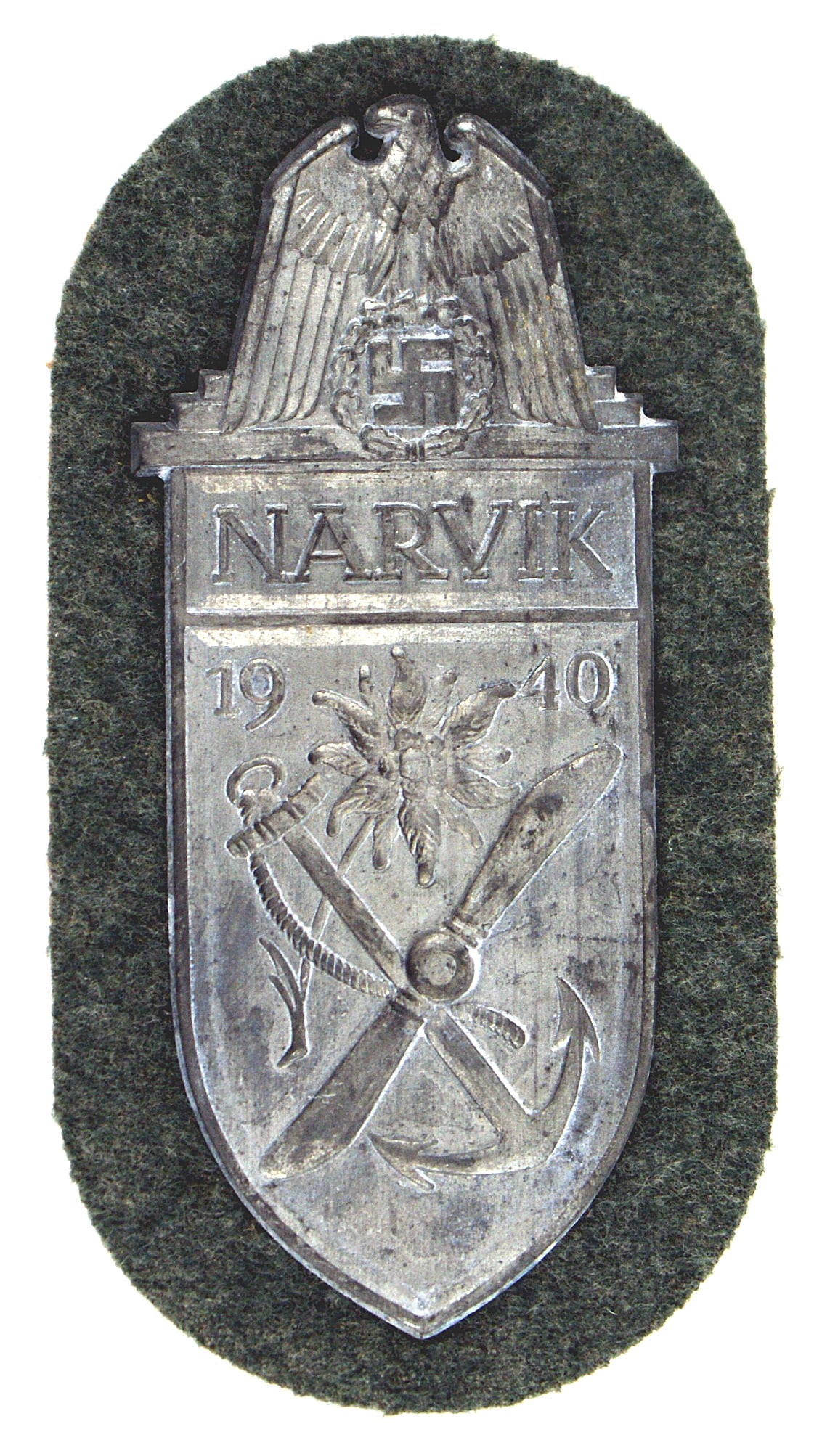 German WWII Army Narvik Shield: B-087 German WWII Army Narvik Shield. Crossed anchor/prop below an edelweiss and 1940. Eagle/swastika and "NARVIK" at top of the shield. With Army feld-grau fabric and paper backing. Traces of silver 