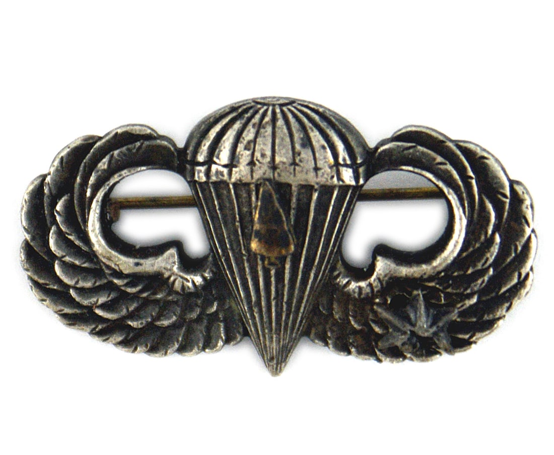 US WWII silver paratrooper wings: B-249 US WWII silver paratrooper wings. Miniature arrowhead (signifies an Airborne landing) and a silver star (represents five Bronze Stars) are attached. Reverse is marked "STERLING". Horizontal pin.