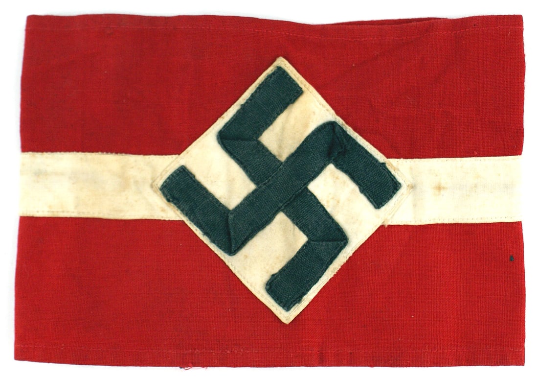 German WWII Hitler Youth Corps armband: H-012 German Third Reich Hitler Youth Corps armband. Black ribbon swastika sewn on a white square which is sewn as a triangle on a red band with a white stripe sewn down the center. Band is 3 5/8". Li